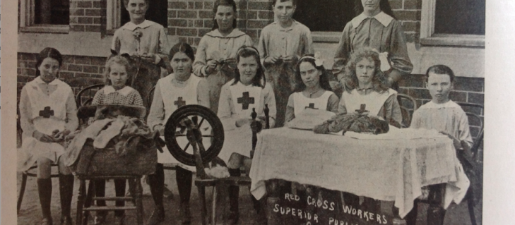 Red Cross workers of Coonamble Superior School with spinning wheel and knitted socks for the war effort. From Education Gazette January 1918