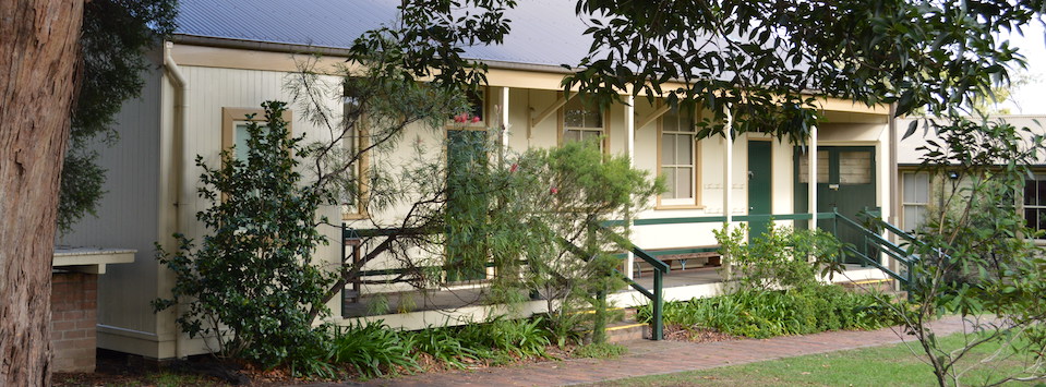 Exterior of wooden school building. Three steps leading up to a long verandah with two classroom doors.