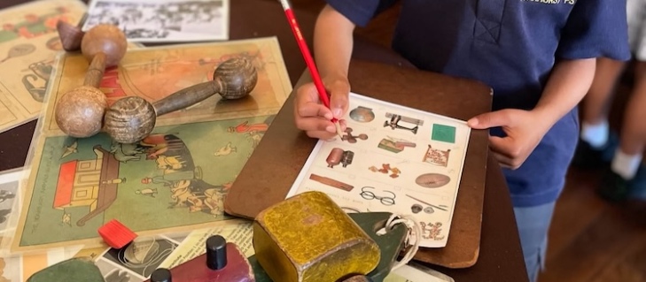 A child with a pencil ticking a photo of an object on a worksheet. It is on a table wiht wooden toys and bone knuckles.